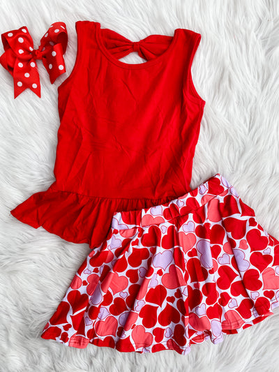 Two piece girls skort set with red peplum top with bow on back and skort with red and pink hearts. 