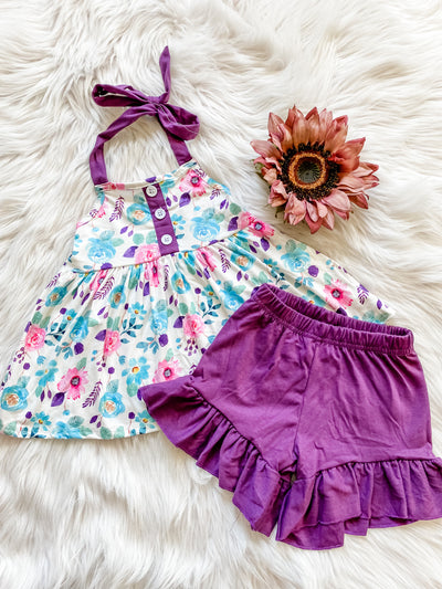 Girls two piece outfit with dainty halter tie top with blue and pink flowers and purple ruffle elastic stretch shorts.