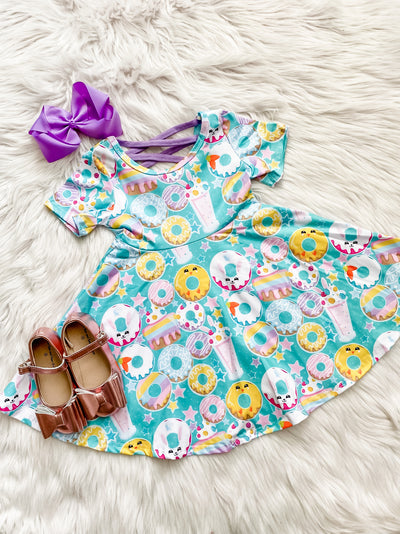 Girls Pastel Donut Print Twirl Dress. Short sleeve dress with criss cross back, a teal background, and all over pastel donut and milkshake print.