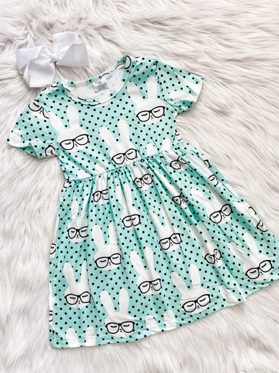 Mint colored short sleeve girls dress with black polka dots covered in white bunnies wearing black glasses. 